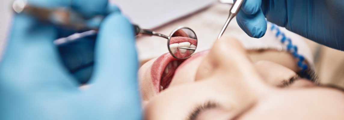 Close-up of woman opening her mouth wide during inspection of oral cavity. Dentist is checking up her teeth using dental tools. Medicine and health care concept. Focus on dental tools. Horizontal shot